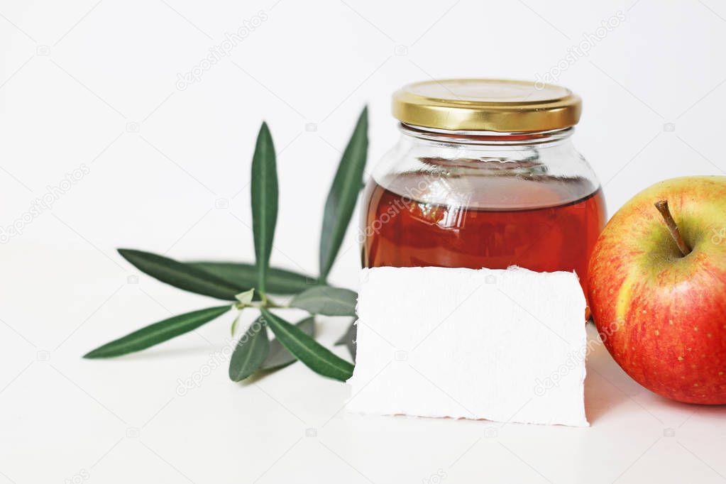 Rosh hashana, Jewish New Year traditional food still life composition. Blank greeting card mockup with honey jar, apple fruit and olive branch on white table background.