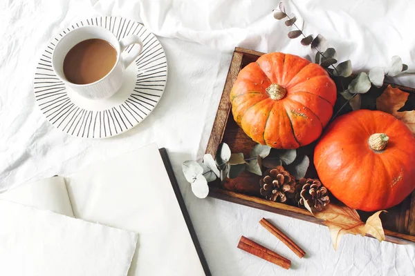 Desayuno de otoño en la composición de la cama. Tarjeta en blanco, maqueta de cuaderno. Copa de café., hojas de eucalipto y calabazas en bandeja de madera. Fondo de sábanas de lino blanco. Acción de Gracias, concepto de Halloween. Plano — Foto de Stock