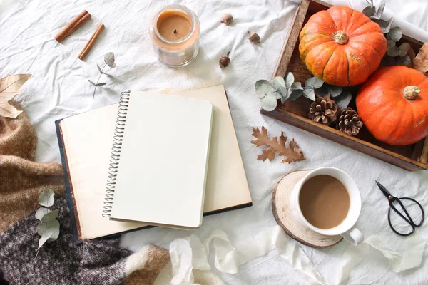 Autumn breakfast in bed composition. Blank notepad, book mockup. Coffee, candle,eucalyptus leaves and pumpkins on wooden tray. White linen bed sheet background. Thanksgiving, halloween. Flat lay, top. — Stock Photo, Image
