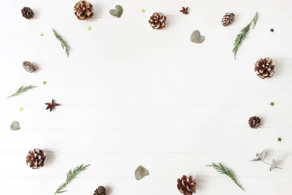 Jul dekorativa sammansättning. Blommig ram av vintergröna juniperus grenar, eucalyptus blad, tall, lärk kottar och glittrande konfetti stjärnor. Vit trä tabellbakgrund. Botaniska mönster. — Stockfoto