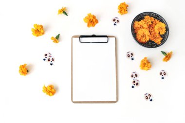 Dia de los Muertos, Meksika gün ölü kompozisyon. Pano, boş kağıt mockup, turuncu tagetes, kadife çiçeği çiçek ve dekoratif kağıt kafatası çıkartmaları. Beyaz masa artalanını. Düz yatıyordu, en iyi görünümü