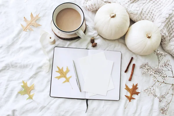 Autumn breakfast in bed composition. Blank cards, notebook mockup. Cup of coffee, white pumpkins, sweater, oak leaves and gypsophila flowers on linen background. Thanksgiving, Halloween. Flat lay. Top