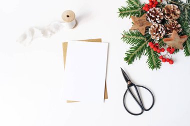 Noel kompozisyon. Boş tebrik kartı, zarf mock-up sahne. Dekoratif köşe. Çam kozalakları, köknar ağacı dalları, kırmızı üvez meyveleri ve beyaz masa arka plan üzerinde ahşap yıldız. Düz yatıyordu, en iyi görünümü.