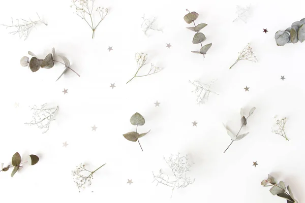 Christmas floral pattern. Winter composition of eucalyptus tree branches, babys breath flowers, Calocephalus brownii and silver confetti stars on white table. Festive background. Flat lay, top view. — Stock Photo, Image