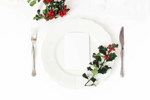 Local de mesa de Natal tradicional. Talheres de prata, ramos de baga azevinho, placa de porcelana e fita de seda. Um maquete de cartas em branco. Conceito de menu de casamento ou restaurante de inverno. Deitado plano, vista superior . — Fotografia de Stock