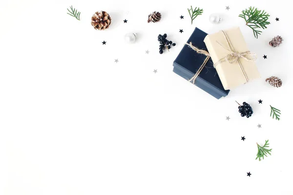 Kerst samenstelling. Decoratieve hoek, banner gemaakt van cypress takken, dennenappels, Kerstmis verpakt geschenken, zwarte bessen en zilveren confetti sterren. Witte tabelachtergrond. Plat lag, top uitzicht. — Stockfoto