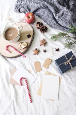 Noel yatak natürmort kompozisyon. Tebrik kartları, Hediyelik Etiketler mockup sahne. Bir fincan kahve, şekerler, hediye kutusu ve ahşap yıldız. Beyaz keten yatak sayfa arka planı. Kış düz yatıyordu, en iyi görünümü.