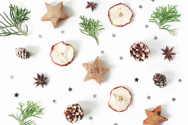 Christmas festliga stil sammansättning. Dekorativa mönster. Kottar, torkade apple frukt, cypress grenar, anis, konfetti och trä stjärnor isolerad på vit trä bakgrund. Platt lekmanna, top view — Stockfoto