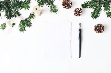 Noel şenlikli kompozisyon. Zarf ve boş kağıt tebrik kartı mockup sahne. Köknar ağacı dalları sınır. Çam kozalakları, ipek kurdele ve kaligrafi kalemi Beyaz ahşap zemin üzerinde. Düz yatıyordu, en iyi görünümü