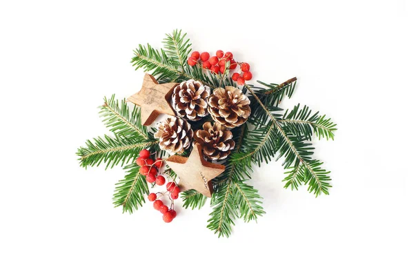 Christmas festliga stil sammansättning. Vinter blomsterarrangemang. Tall kottar, fir trädgrenar, röda Rönnbär och trä stjärnor och på vitt bordsbakgrund. Platt lekmanna, top view. — Stockfoto