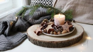 Noel rahat sakin sahne. Yanan mum ayakta pencere yakınındaki. Parlak Noel ışıkları. Çam kozalakları, fındık ve ahşap yıldız doğal dekorasyon. Yün şal üzerinde köknar ağacı dalı. Loopable.