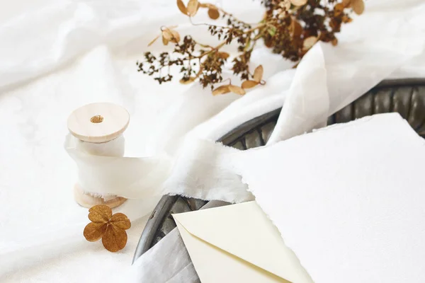 Inverno, casamento de outono, composição de mesa de aniversário. Cena de maquetes de papelaria. Cartão, envelope, flores secas de hortênsia e fita de seda na velha bandeja vintage. Fundo de tecido de seda branca . — Fotografia de Stock