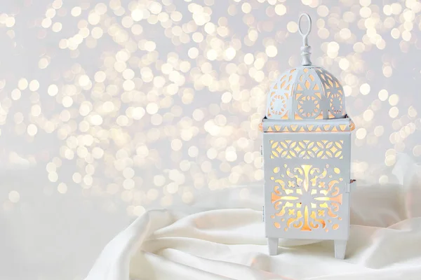 Dekorativ vit marockansk, arabiska lykta på silk textil kasta. Brinnande ljus, glittrande bokeh lampor. Gratulationskort för muslimska gemenskapen heliga månaden Ramadan Kareem. Festlig bakgrund. — Stockfoto