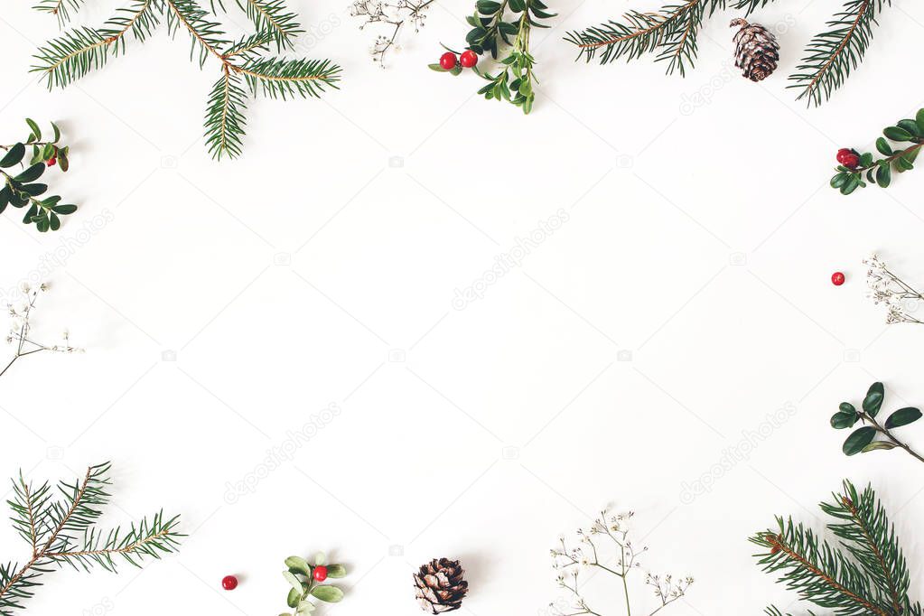 Christmas floral frame, decorative border. Winter composition of red cranberry branches, babys breath flowers, spruce tree branches and larch cones on white table. Festive background. Flat lay, top