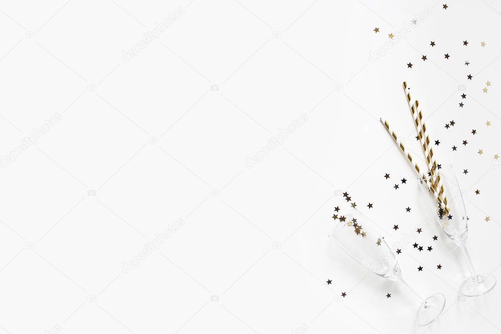 Happy New Year composition. Champagne glasses with golden confetti stars and drinking straws isolated on white table background. Celebration, party concept. Flat lay, top view. Empty copy space.