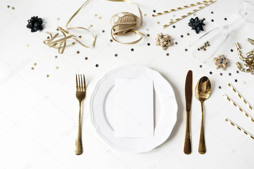 New Year, Christmas styled black and gold table setting with plate, cutlery, confetti stars and champagne wine glass. Party decoration. Restaurant menu blank card mockup. Flat lay, top view.