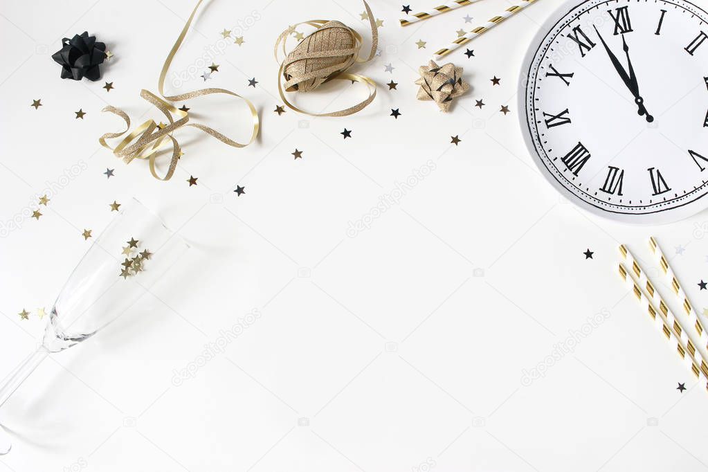 New Year still life composition with golden confetti stars, wine glass, drinking straws and clock plate. Party decoration, celebration concept. Flat lay, top view. Empty space.