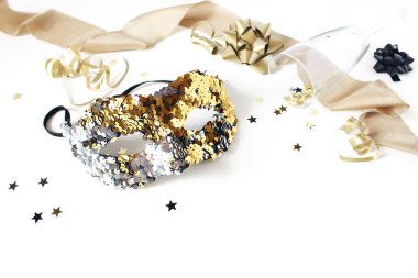 Karnaval maskesi, siyah ve altın konfeti yıldızları, kurdeleler ve şarap kadehleriyle yeni yıl şenliği. Parti dekorasyonu, kutlama konsepti, seçici odak.