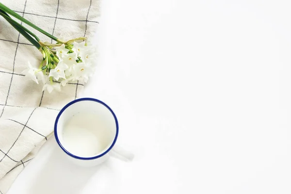 Scena di colazione con tazza di latte, strofinaccio e bouquet di narcisi, fiori di narciso su sfondo bianco. Composizione primaverile, concetto pasquale. Posa piatta, vista dall'alto. Immagine stock in stile . — Foto Stock