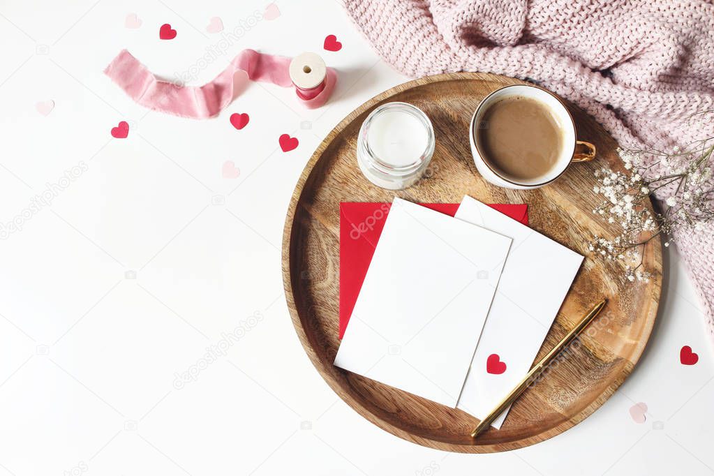 Breakfast still life scene. Cup of coffee, Gypsophila flowers, paper hearts confetti, candle and blank greeting card mockup on wooden tray. Valentines day, wedding or love concept. Flat lay, top view.