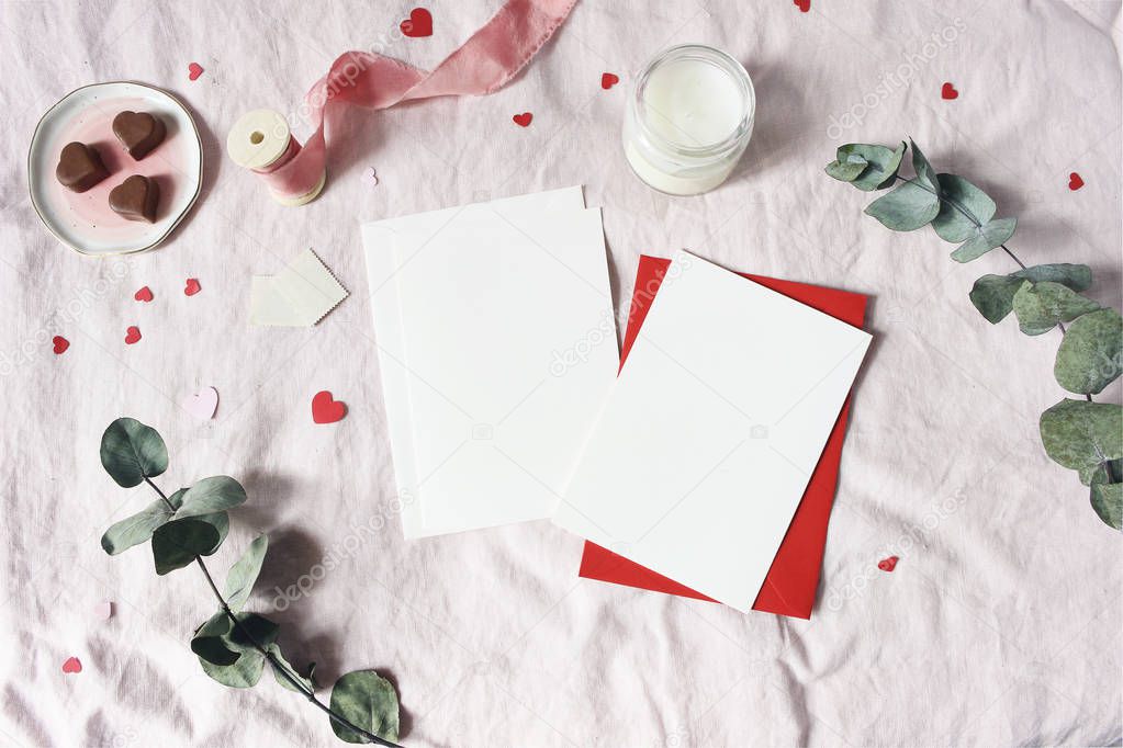 Valentines day, wedding stationery mockup scene. Candle, hearts confetti, chocolate, eucalyptus branch and blank greeting cards, envelopes. Pink linen background. Love concept. Flat lay, top view.