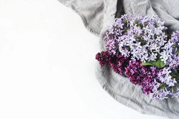 Pâques style photo de stock. Scène féminine de printemps, composition florale. Bannière décorative, coin fait de belles fleurs lilas violettes sur une serviette en lin. Fond de table blanc. Couché plat, vue du dessus . — Photo