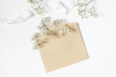 Stok fotoğraf tarz. Kadınsı düğün masaüstü mockup babys nefes Gypsophila çiçekler, saten kurdele ve boş craft Kağıt zarf mockup beyaz masa arka plan üzerinde. Üstten görünüm, düz yatıyordu.