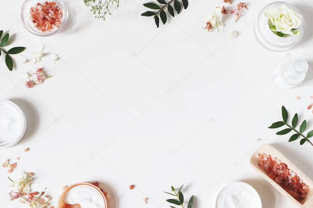 Styled beauty frame, web banner. Skin cream, tonicum bottle, dry flowers, leaves, rose and Himalayan salt. White table background. Organic cosmetics, spa concept. Empty space, flat lay, top view.