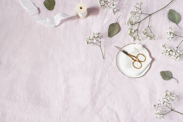 Styled stock photo. Feminine wedding desktop scene. Babys breath Gypsophila flowers, dry green eucalyptus leaves, satin ribbon, golden scissors on pink linen background. Empty space. Top view. — Stock Photo, Image