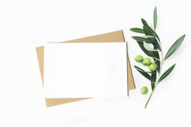 Kadınsı kırtasiye, masaüstü mock-up sahne. Boş yatay tebrik kartı ve zanaat zarf ile zeytin dalı. Beyaz masa artalanını. Düz yatıyordu, en iyi görünümü.