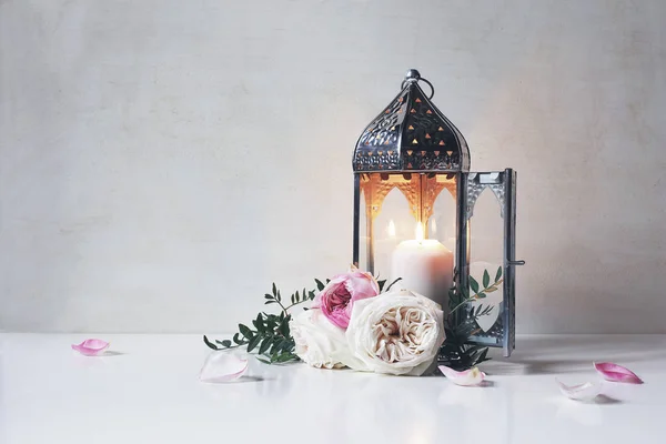 Vintage silver Moroccan, Arabic lantern with glowing candle, green branches, rose flowers and pink petals on white table background. Greeting card for Muslim holiday Ramadan Kareem. Shaby wall. — Stock Photo, Image