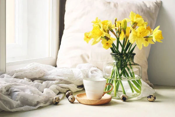 Cozy Easter, spring still life scene. Cup of coffee, wooden plate, quail eggs and vase of flowers on windowsill. Floral composition with yellow daffodils, narcissus. Vintage feminine styled photo. — Stock Photo, Image