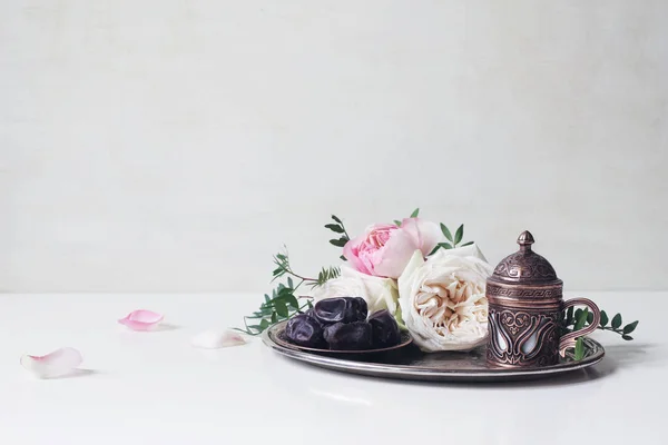 Cartão de saudação Ramadan Kareem, convite. Prato com frutas datas, xícara de café de bronze, rosas rosa e ramos verdes na bandeja de prata velha. Fundo da mesa branca. Jantar muçulmano Iftar. Banner de Eid ul Adha . — Fotografia de Stock