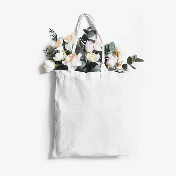 Mock-up scene of blank shopping canvas tote bag with pink tulips, daffodils flowers and eucalyptus isolated on white backfound. Spring, Easter sale. Eco friendly, zero waste concept. Flat lay, square. — Stock Photo, Image