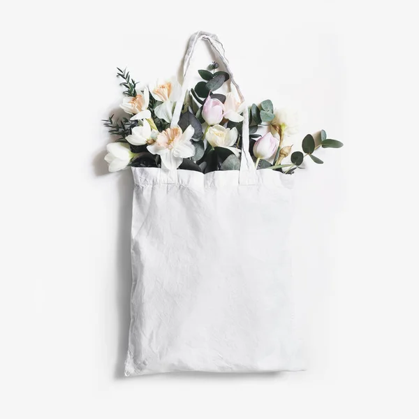 Cena recheada de sacola de lona de compras em branco com tulipas cor-de-rosa, flores de narcisos e eucaliptos isolados em fundo branco. Primavera, venda de Páscoa. Eco amigável, zero conceito de resíduos. Flat lay, quadrado . — Fotografia de Stock