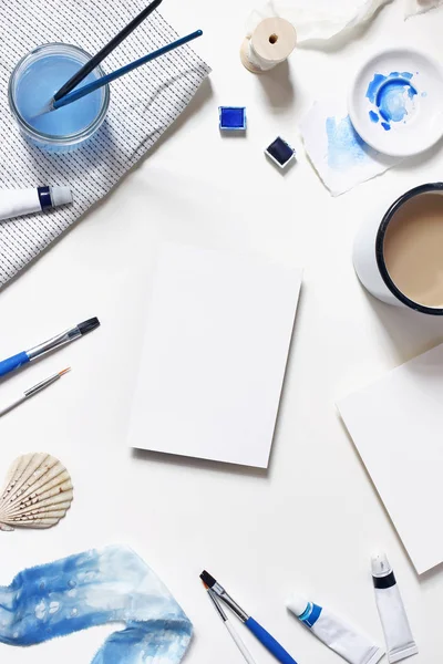 Aquarela, óleo, tubos de tinta de cor acrílica, escovas, paleta, xícara de café e maquetes de papel em branco isolados na mesa branca. Material de arte cena. Fundo criativo. Colocação plana, vista superior, vertical . — Fotografia de Stock