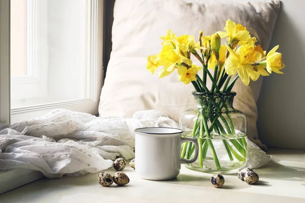 Cozy Easter, spring still life scene. Mug of coffee, wooden plate, quail eggs and vase of flowers on windowsill. Floral composition with yellow daffodils, narcissus. Vintage feminine styled photo. — Stock Photo, Image