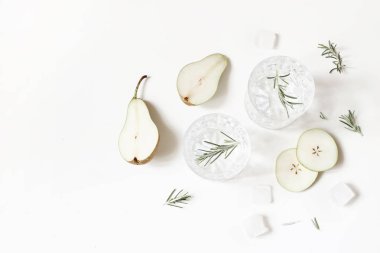 Soğuk armut kokteyller, soda ile iki bardak alkol içecekler, meyve dilimleri, buz küpleri ve biberiye otlar beyaz masa arka plan üzerinde izole bırakır. Yaz ferahlığı konsepti. Düz döşeme, üst görünüm.