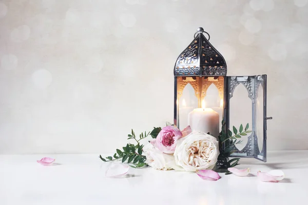 Festive greeting card, invitation for Muslim holiday Ramadan Kareem.Vintage Moroccan lantern with glowing candle, green branches, pink roses flowers and floral petals on table. Glittering bokeh lights — Stock Photo, Image