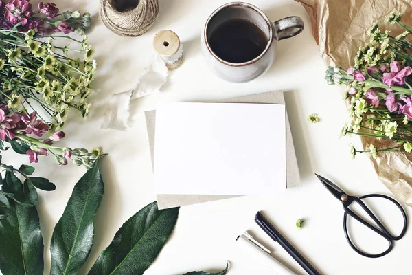 Floral lifestyle, stationery scene. Mums, matthiola flowers, aralia leaf, cup of coffee and vintage scissors on white table. Blank greeting card mockup. Floristry business concept. Flat lay, top view. — Stock Photo, Image