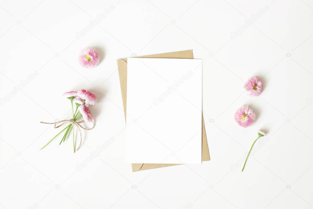 Feminine stationery, desktop mock-up scene. Vertical blank greeting card, craft paper envelope and daisy bouquet and flowers isolated on white table background. Flat lay, top view. Rustic composition.