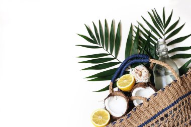 Saman sepet çanta, yemyeşil palmiye yaprakları, limon, hindistan cevizi ve beyaz arka plan üzerinde izole su cam şişe ile Yaz natürmort kompozisyon. Tropikal tasarım, piknik konsepti. Düz döşeme, üst görünüm.
