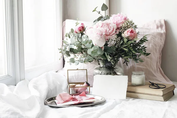 Spring, summer wedding still life scene. Blank paper card mockup, old books and linen pillow at windowsill. Vintage feminine floral composition. Bouquet of pink roses, peony flowers and eucalyptus. — Stock Photo, Image