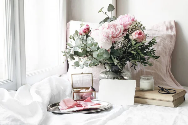 Primavera, verano boda naturaleza muerta escena. Tarjeta de papel en blanco maqueta, libros viejos y almohada de lino en el alféizar de la ventana. Composición floral femenina vintage. Ramo de rosas rosadas, flores de peonía y eucalipto . — Foto de Stock