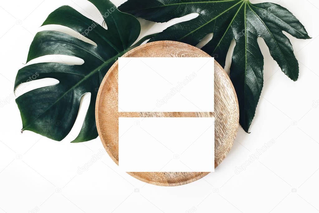 Blank white business cards mockups, wooden plate, aralia and monstera leaf isolated on white table backgound. Modern template for branding identity. Tropical design. Wedding stationery. Flat lay, top