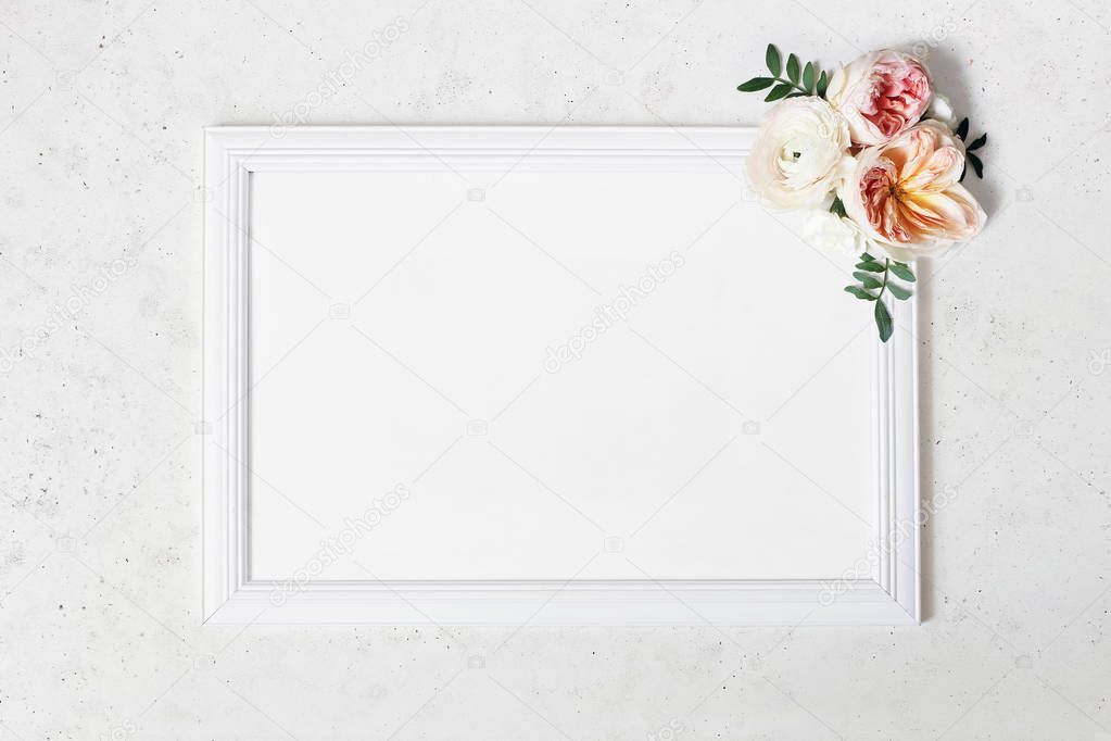 Wedding, birthday sign board mock-up scene. Blank white wooden frame. Decorative floral corner. Green leaves, pink English roses and ranunculus flowers. Concrete table background. Flat lay, top view