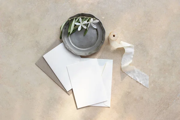 Summer wedding stationery mock-up scene. Blank greeting cards, envelopes, silver plate with olive branch and white flowers and silk ribbon. Marble background in sunlight, shadows. Flat lay, top view. — Stock Photo, Image