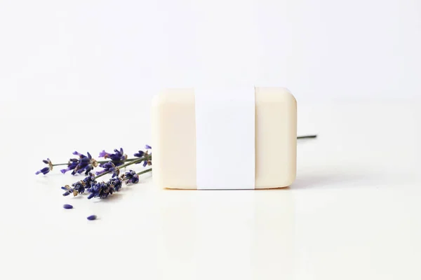 Nahaufnahme von handgemachter Kräuterseife in leerer Papieretikettenverpackung und einem Bund Lavendelblüten auf weißem Tischhintergrund. Wellness-Konzept. Skin Produkt Attrappe Szene. kosmetisches Produkt. — Stockfoto