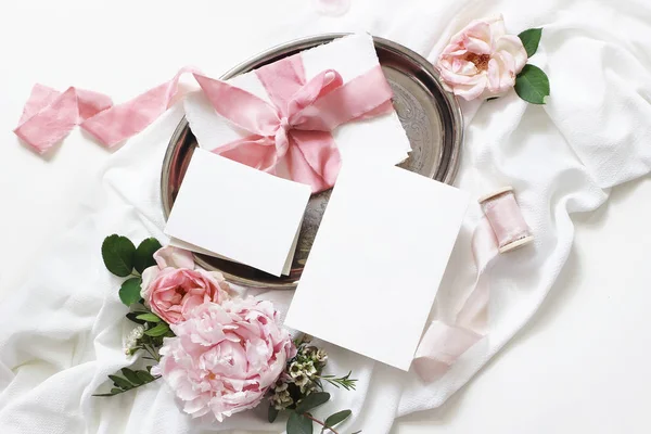 Matrimonio femminile, scena del modello di compleanno. Biglietti di auguri in carta bianca, busta, eucalipto, rose rosa, fiori di peonia e nastri su sfondo bianco. Luce, gioco di ombre. Posa piatta, vista dall'alto — Foto Stock