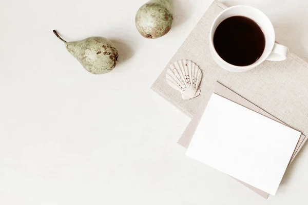 Papeterie féminine, maquettes de bureau. Carte de vœux vierge, enveloppe artisanale, tasse de café, coquillage, poires et vieux livres. Fond de table blanc. Couché à plat, vue de dessus. Été, composition d'automne . — Photo